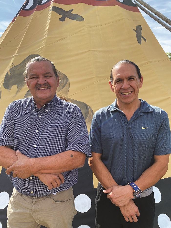 Chief Henry Red Cloud, executive director of Red Cloud Renewable, stands next to John Red Cloud, its managing director, in front of a teepee.